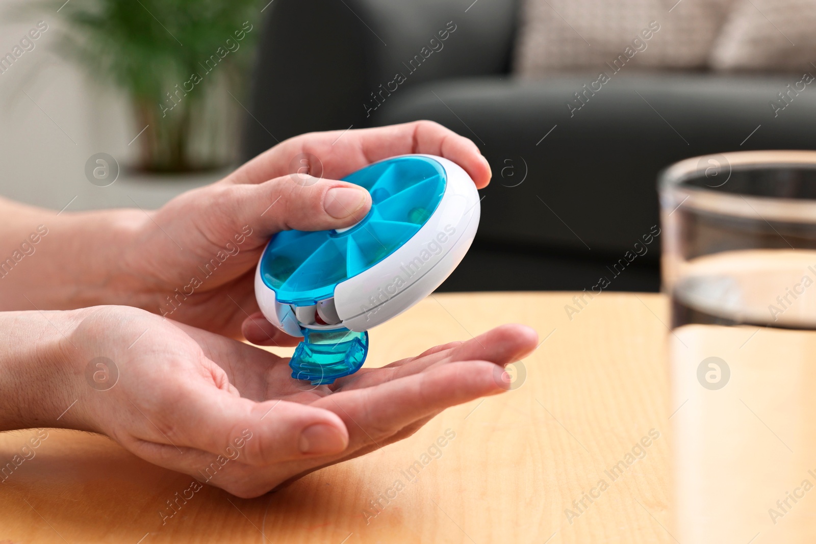 Photo of Woman with pills, organizer and glass of water at light wooden table, closeup