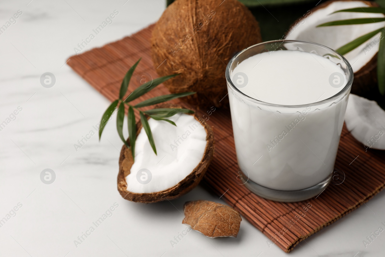 Photo of Glass of delicious vegan milk, coconut pieces and palm leaves on white marble table