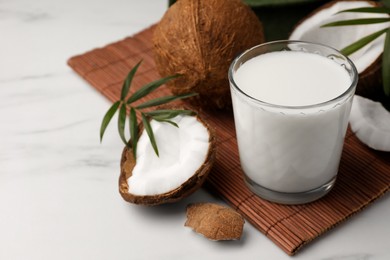 Photo of Glass of delicious vegan milk, coconut pieces and palm leaves on white marble table