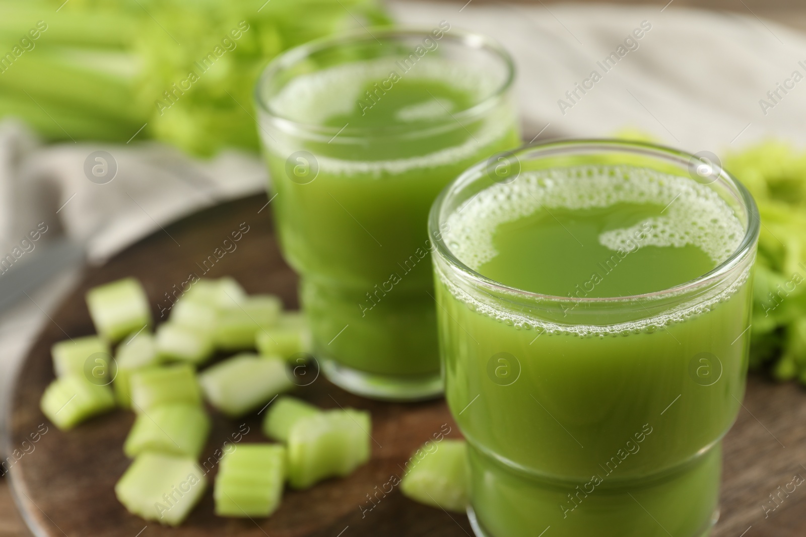 Photo of Glasses of delicious celery juice and vegetables on wooden board, closeup