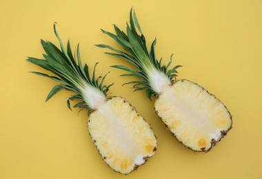 Photo of Halves of ripe pineapple on yellow background, flat lay