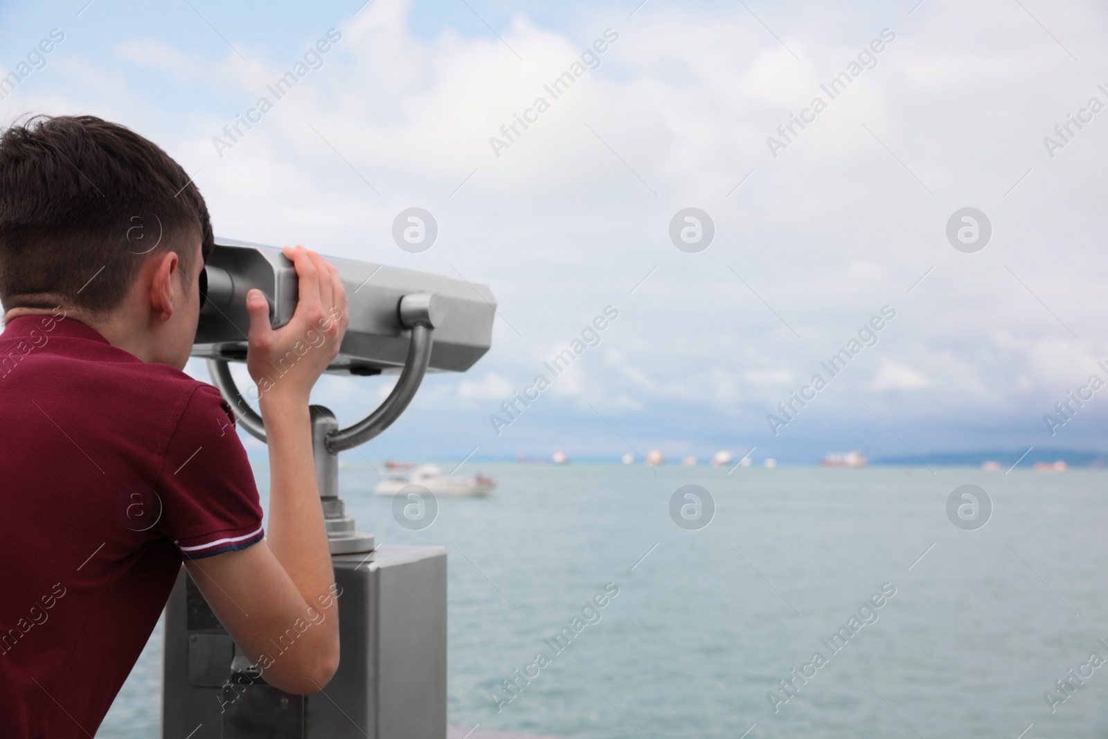 Photo of Teenage boy looking through mounted binoculars at mountains. Space for text