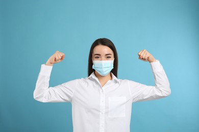 Photo of Woman with protective mask showing muscles on light blue background. Strong immunity concept