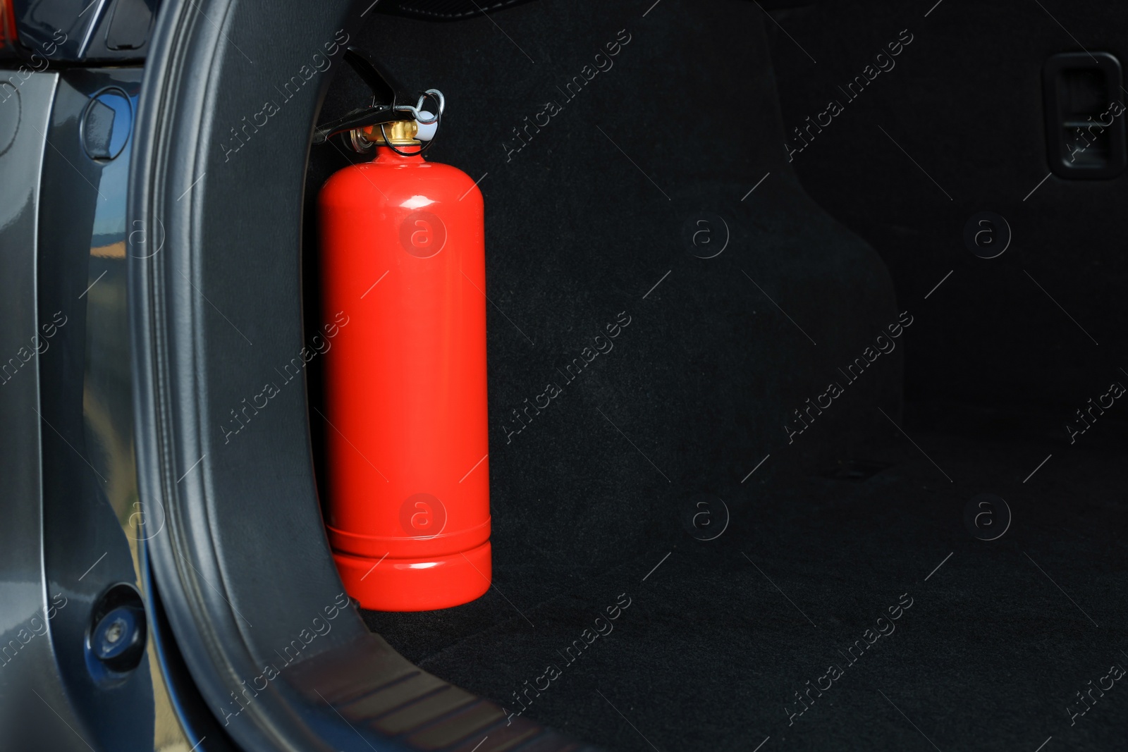 Photo of Red fire extinguisher in trunk, space for text. Car safety equipment