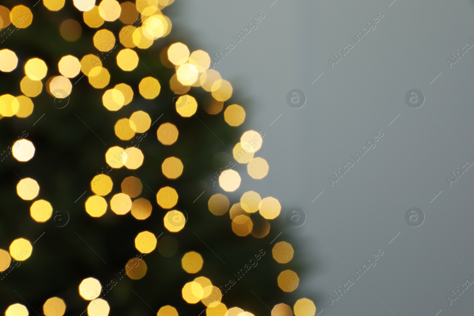 Photo of Blurred view of beautiful fir tree with Christmas lights on grey background, closeup. Space for text