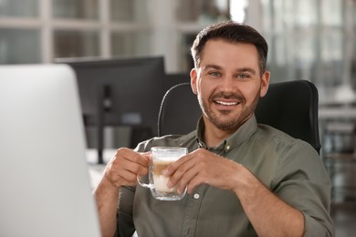 Happy man with cup of coffee working on modern computer in office