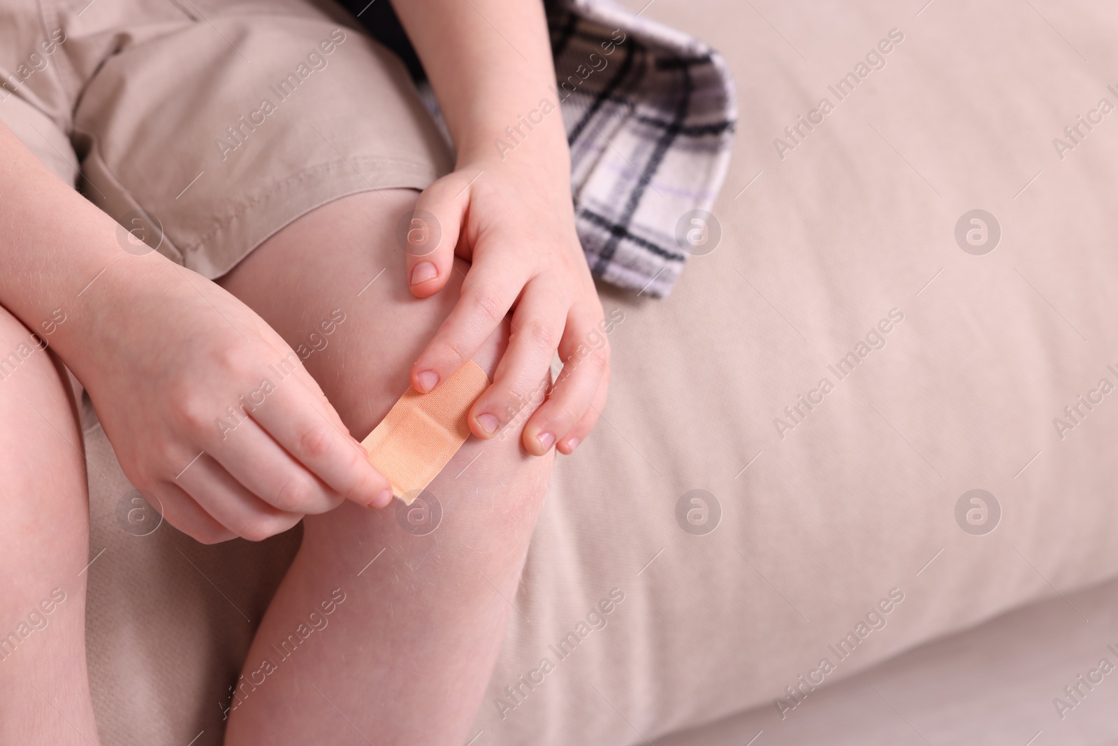 Photo of Little boy putting sticking plaster onto knee on sofa, closeup. Space for text