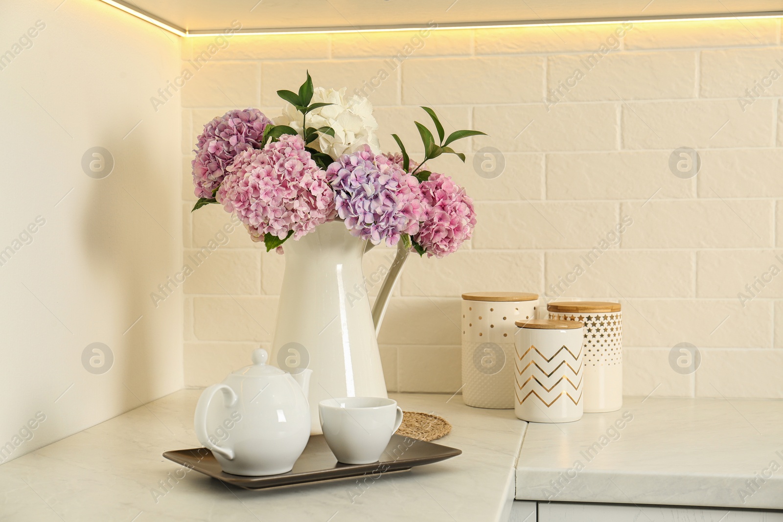 Photo of Beautiful bouquet of hydrangea flowers and tea on light countertop