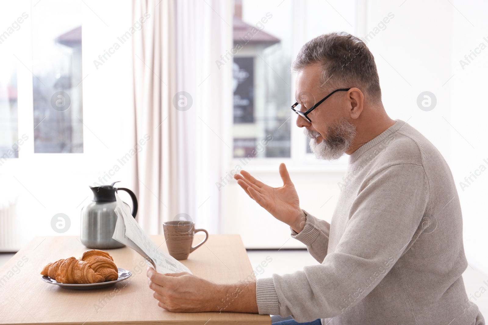 Photo of Senior man reading newspaper at table