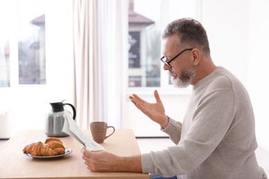 Photo of Senior man reading newspaper at table