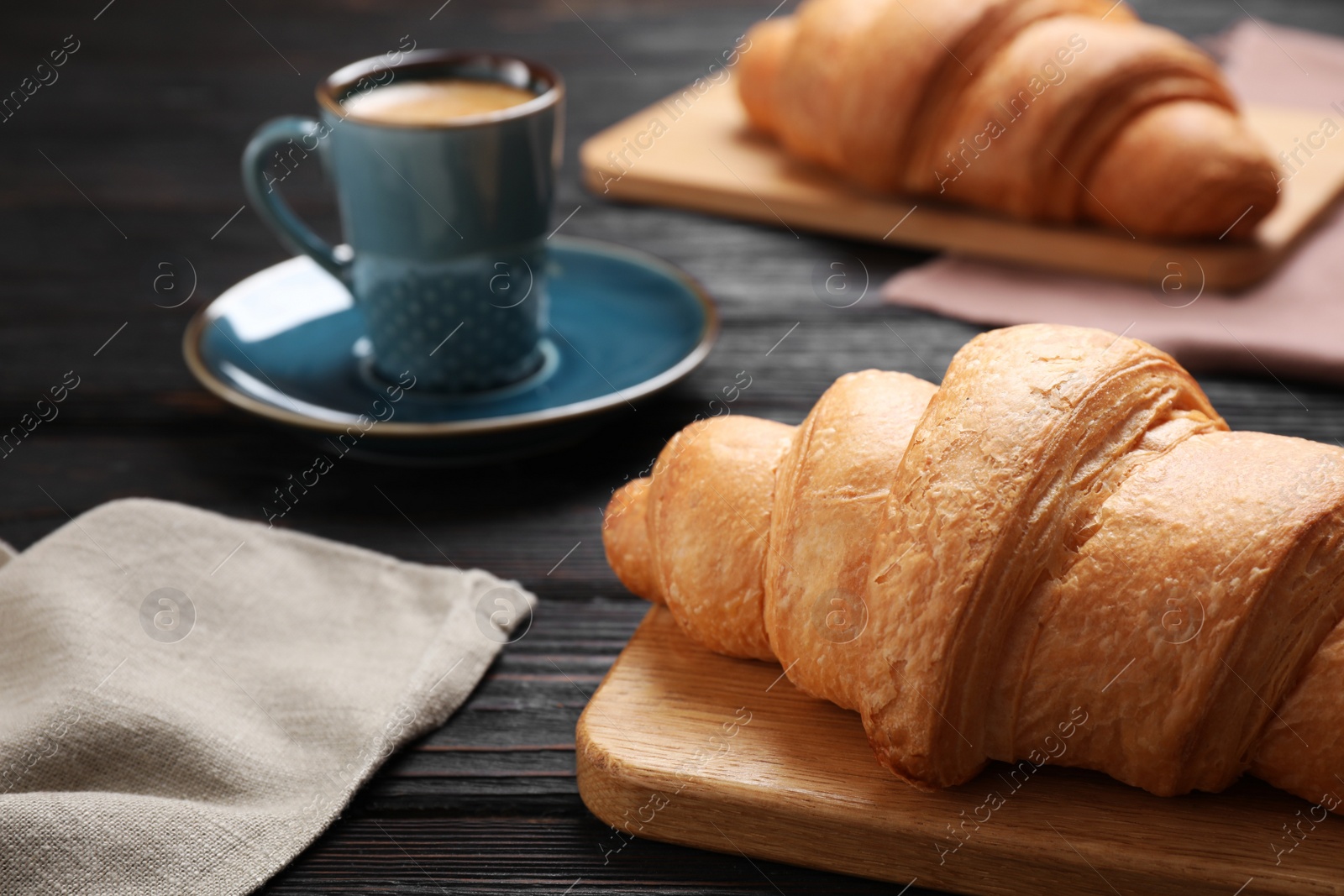 Photo of Tasty fresh croissants and coffee on black wooden table, closeup