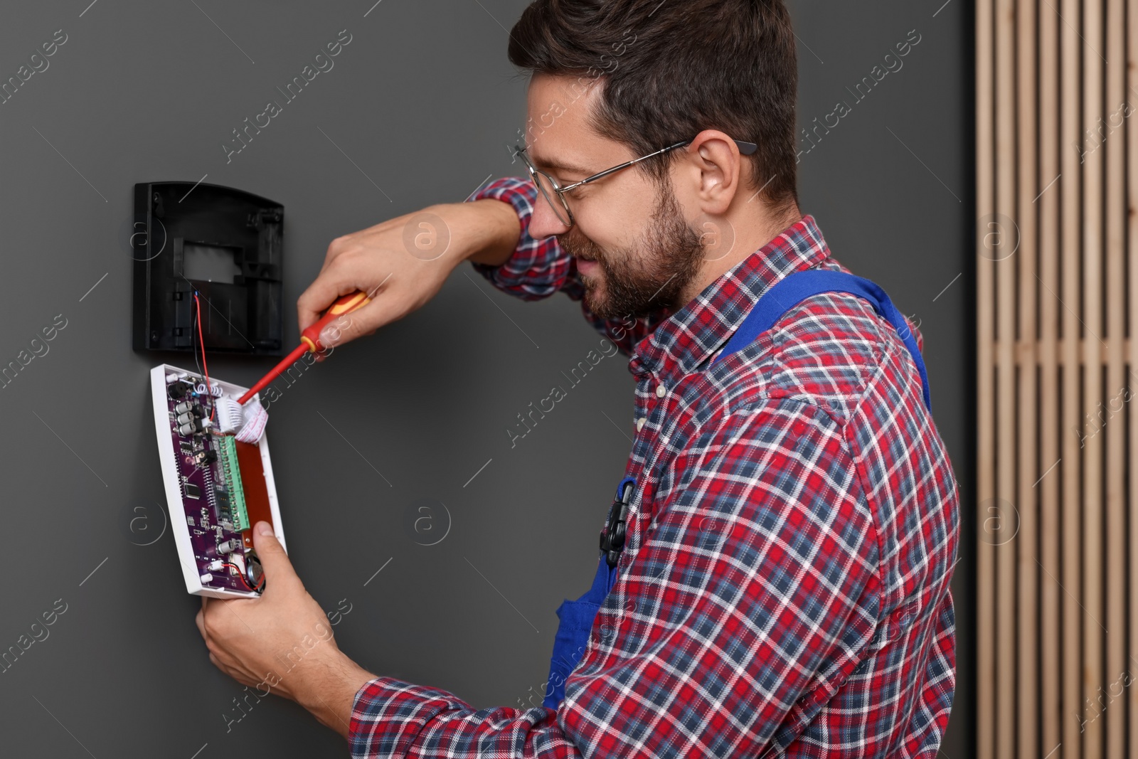 Photo of Technician installing home security alarm system on gray wall indoors