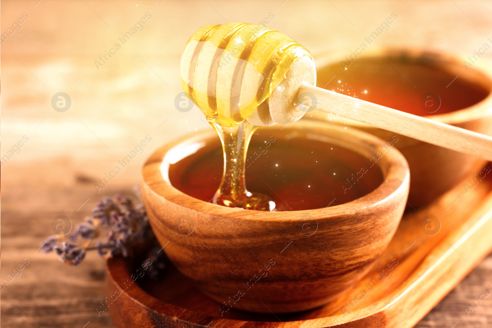 Image of Natural honey dripping from dipper into wooden bowl on table under sunlight, closeup