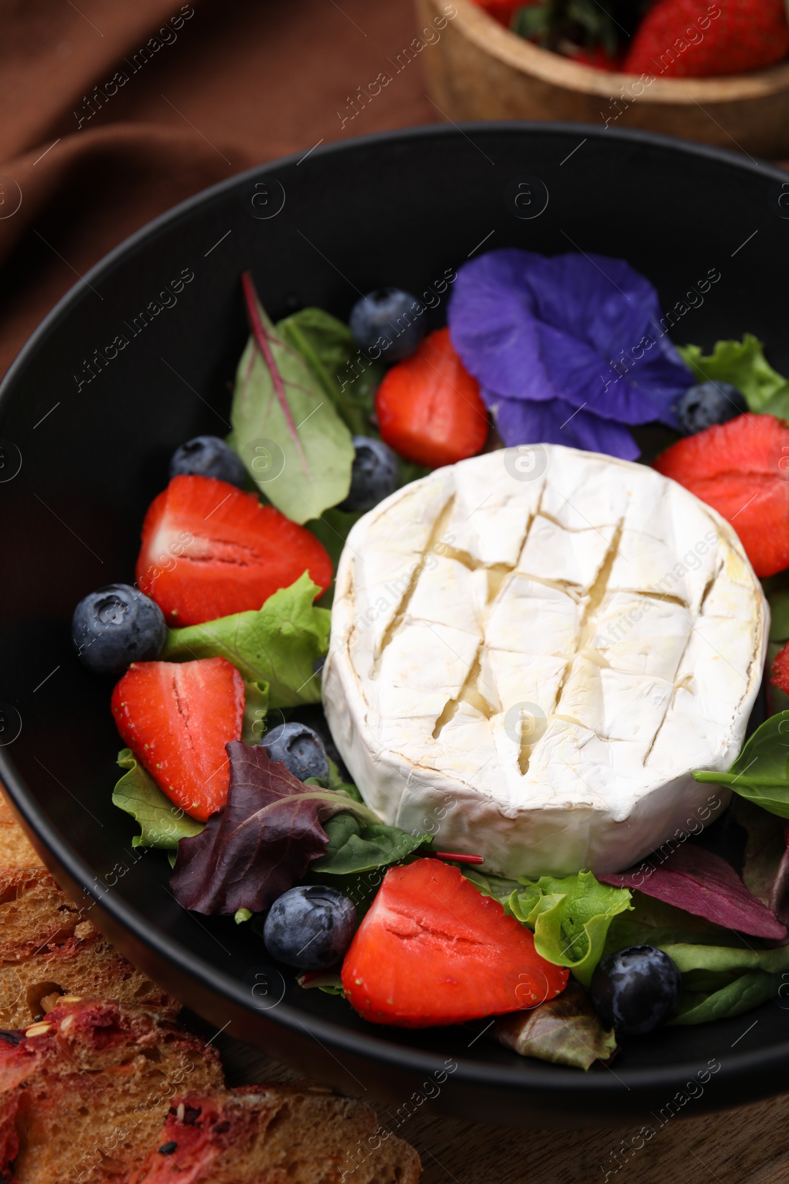 Photo of Delicious salad with brie cheese, blueberries and strawberries on table