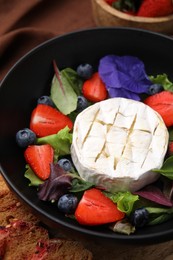 Delicious salad with brie cheese, blueberries and strawberries on table