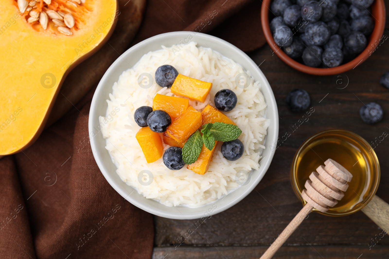 Photo of Bowl of delicious rice porridge with blueberries, pumpkin and honey on wooden table, flat lay