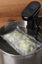 Photo of Thermal immersion circulator and vacuum packed broccoli in pot against wooden background. Sous vide cooking