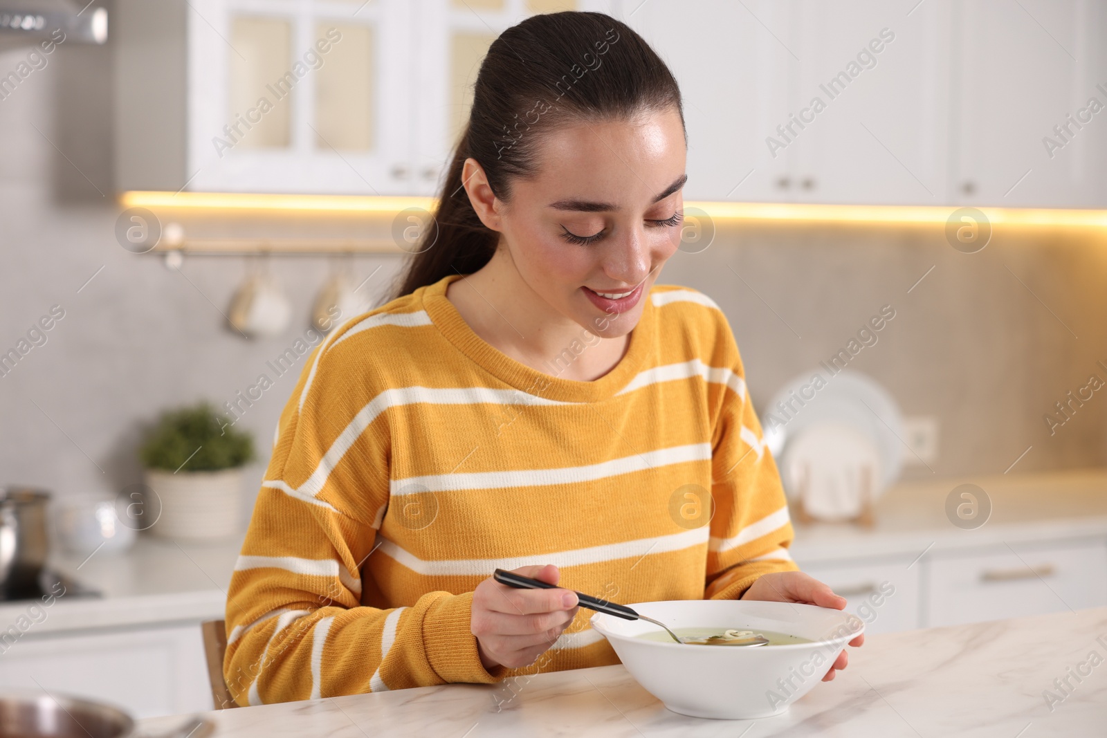 Photo of Woman eating tasty soup at white table in kitchen