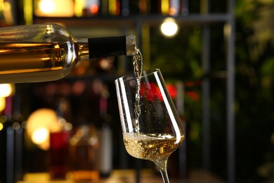 Photo of Pouring white wine from bottle into glass on blurred background, closeup