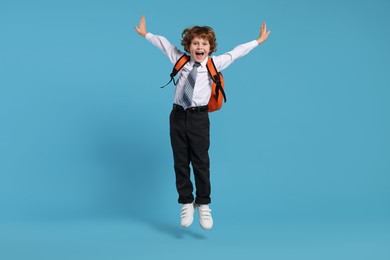 Photo of Happy schoolboy with backpack jumping on light blue background