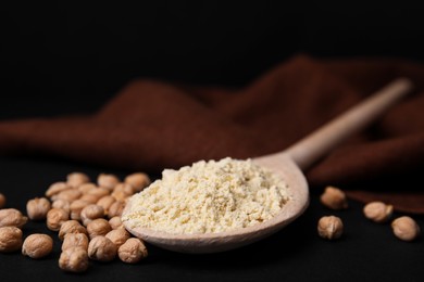 Photo of Spoon with chickpea flour and seeds on black table, closeup. Space for text
