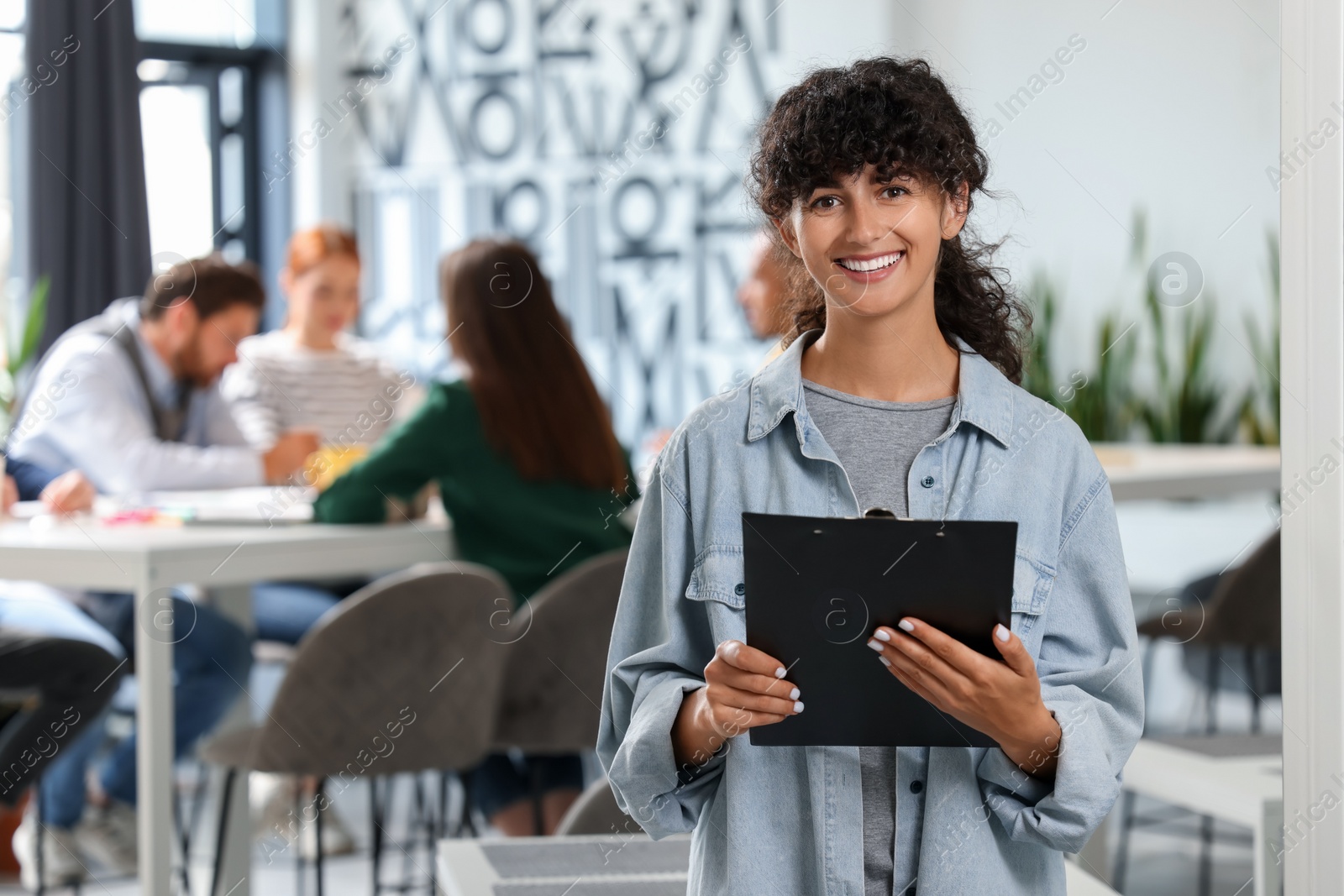 Photo of Team of employees working together in office. Happy woman with clipboard indoors