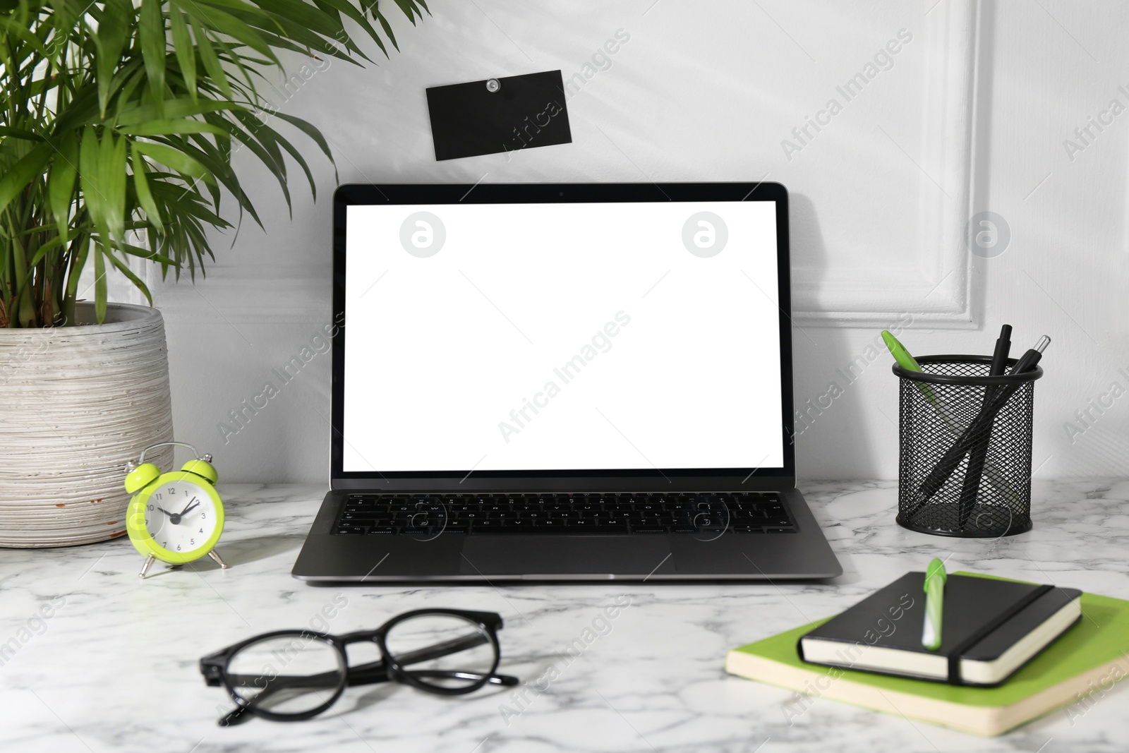 Photo of Office workplace with computer, glasses, houseplant and stationery on marble table near white wall