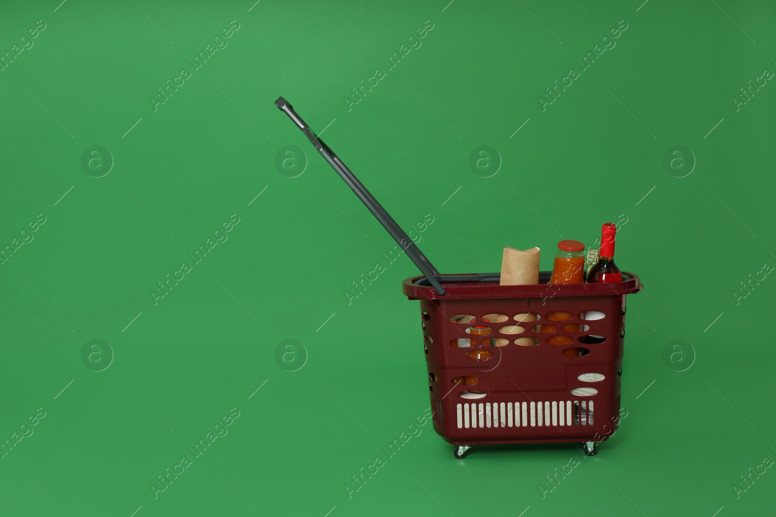 Photo of Shopping basket full of different products on green background. Space for text