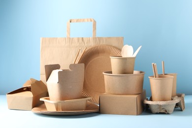 Photo of Eco friendly food packaging. Paper containers, tableware and bag on white table against light blue background