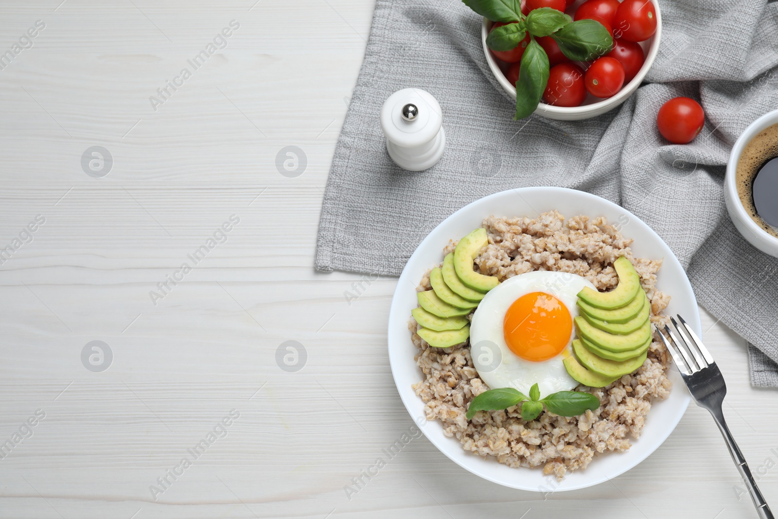 Photo of Delicious boiled oatmeal with fried egg and avocado served on white wooden table, flat lay. Space for text