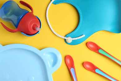 Photo of Set of colorful plastic dishware and silicone bib on yellow background, flat lay. Serving baby food