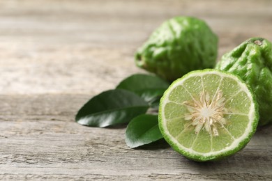 Photo of Fresh ripe bergamot fruits with green leaves on wooden table, closeup. Space for text