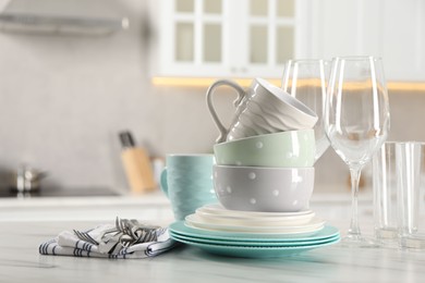 Many different clean dishware, cutlery, glasses and cups on white marble table in kitchen