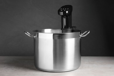 Photo of Sous vide cooker in pot on light grey table. Thermal immersion circulator