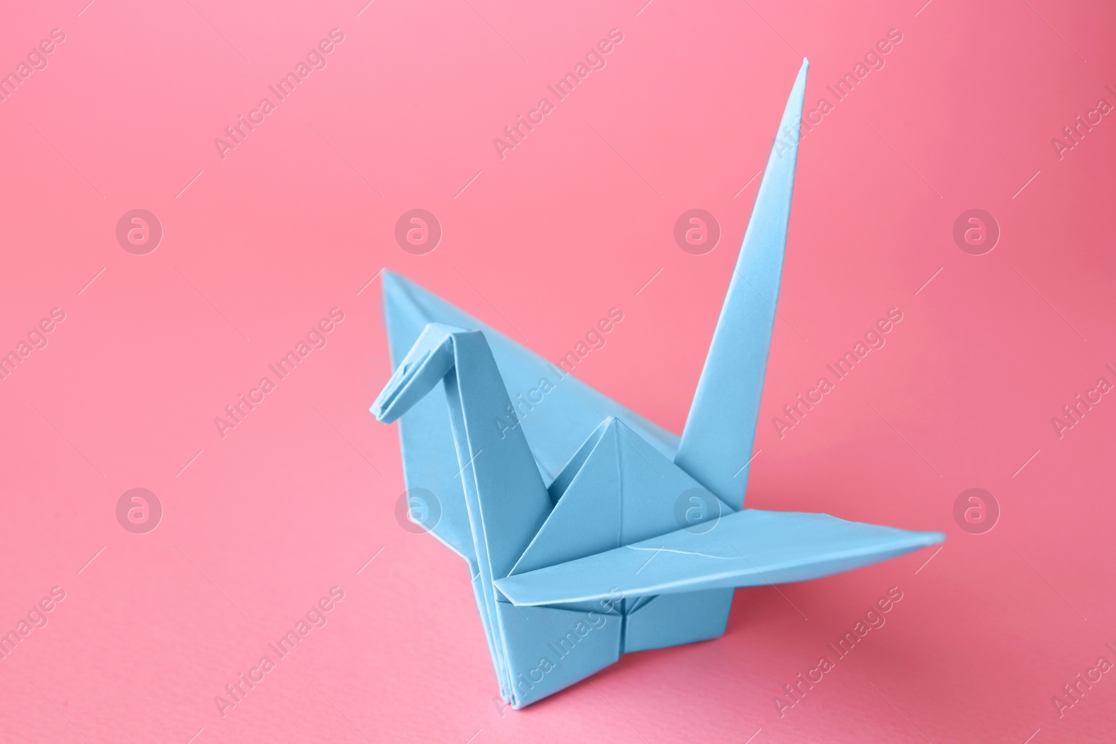 Photo of Origami art. Handmade paper crane on pink background, closeup