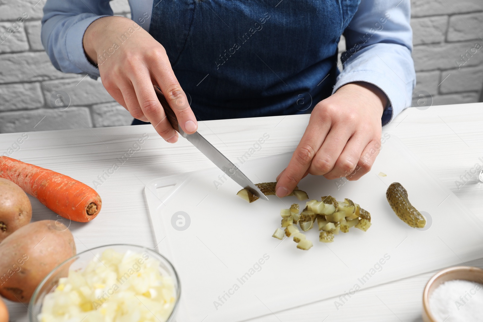 Photo of Woman cutting pickled cucumbers at white wooden table, closeup. Cooking vinaigrette salad