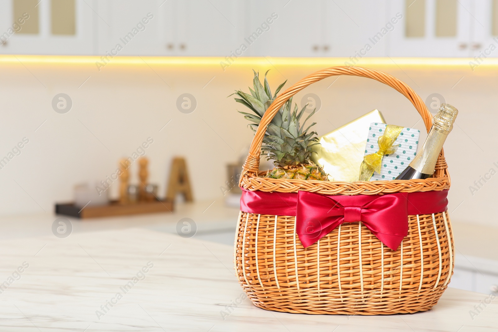 Photo of Wicker basket full of gifts on wooden table in kitchen. Space for text