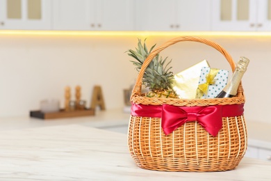 Wicker basket full of gifts on wooden table in kitchen. Space for text