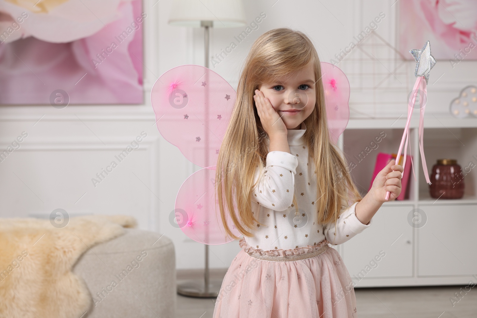 Photo of Cute little girl in fairy costume with pink wings and magic wand at home, space for text