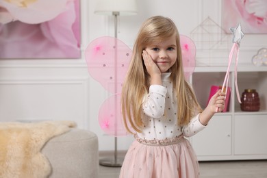 Cute little girl in fairy costume with pink wings and magic wand at home, space for text