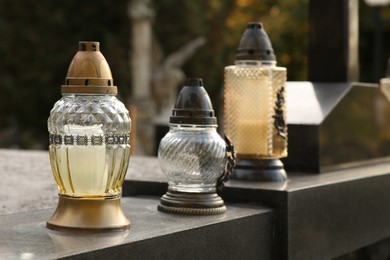 Photo of Different grave lanterns on granite tombstone outdoors, space for text. Funeral ceremony