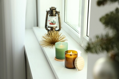 Beautiful burning candles and lantern shaped snow globe on window sill. Christmas decor