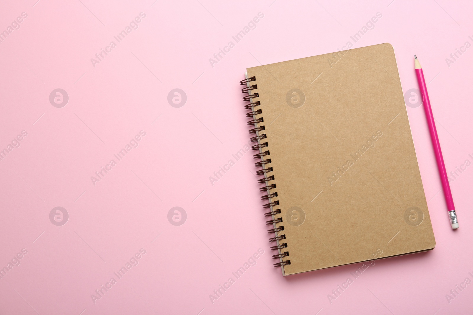 Photo of Notebook and pencil on pink background, top view. Space for text