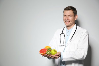 Photo of Nutritionist with fresh fruits on light grey background. Space for text