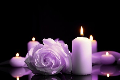 Image of Violet rose and burning candle on black mirror surface in darkness, closeup. Funeral attributes