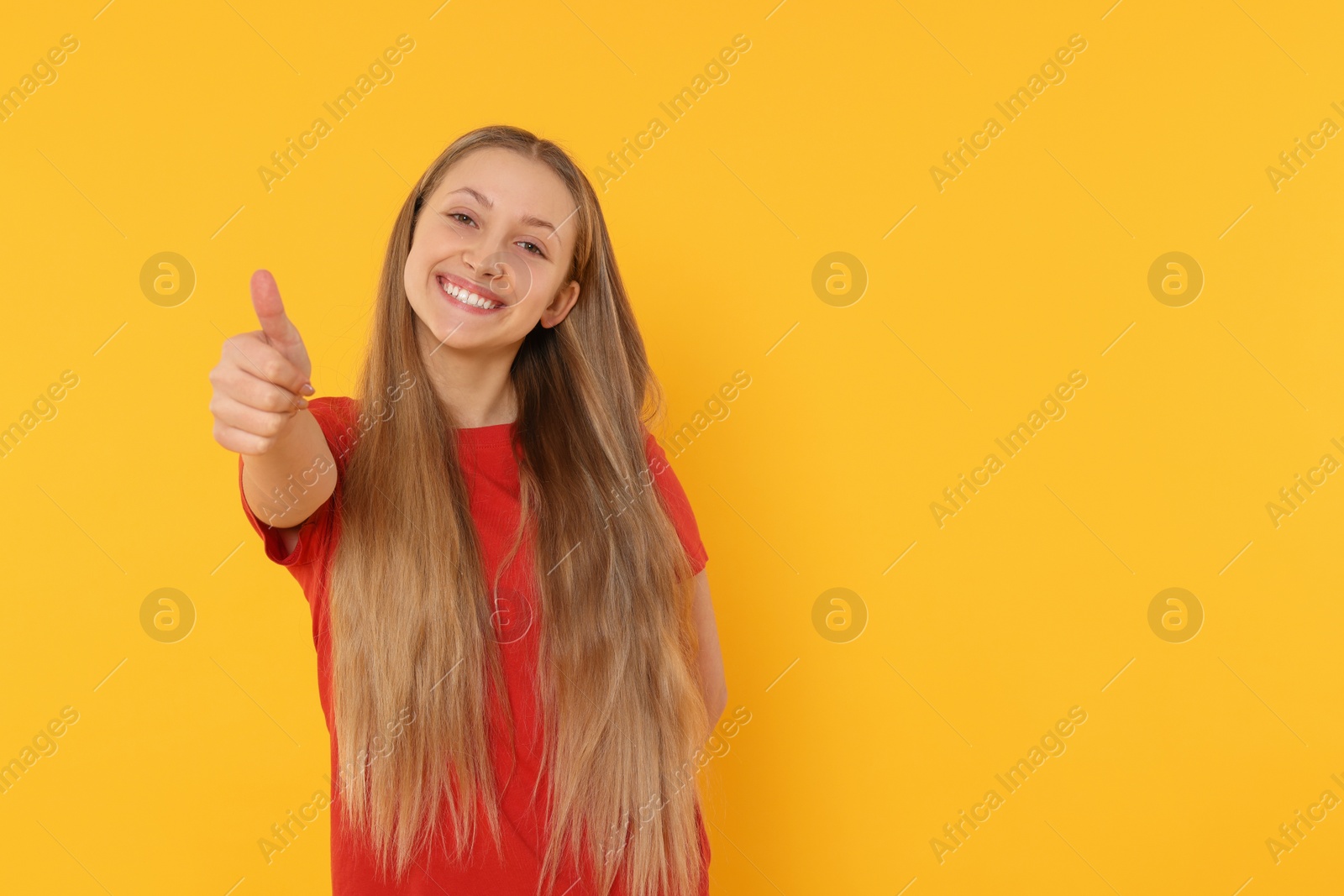 Photo of Teenage girl showing thumb up on orange background. Space for text