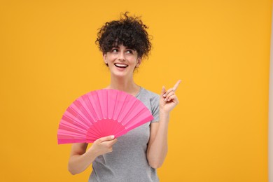 Photo of Happy woman holding hand fan on orange background. Space for text