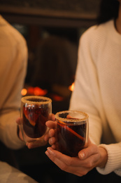 Photo of Couple with tasty mulled wine near fireplace indoors, closeup