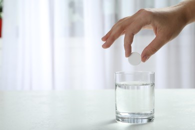 Photo of Woman putting tablet into glass of water indoors, space for text