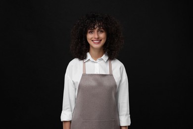 Photo of Happy woman wearing kitchen apron on black background. Mockup for design